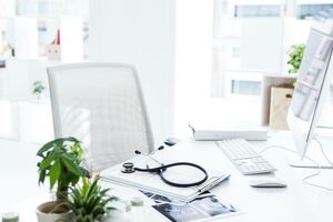 Schreibtisch mit Klemmbrett, Stethoskop, Röntgenbildern und PC.