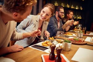 Eine Frau und ein Mann beim gemeinsamen Essen in einem Restaurant, wobei der Mann dabei ist, etwas mit seiner Gabel vom Teller der Frau zu nehmen. Die Frau lacht.