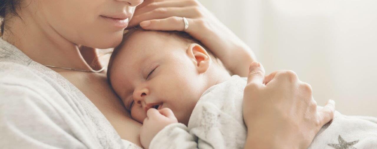 Eine junge Frau, die sich ihr Baby an die Brust hält. Eine Hand am Rücken, die andere am Kopf des Babys.