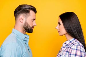 Mann mit dunklen Haaren und Bart und Frau mit langen dunklen Haaren, die sich ins Seitenprofil gedreht gegenseitig in die Augen schauen. Gelber Hintergrund.